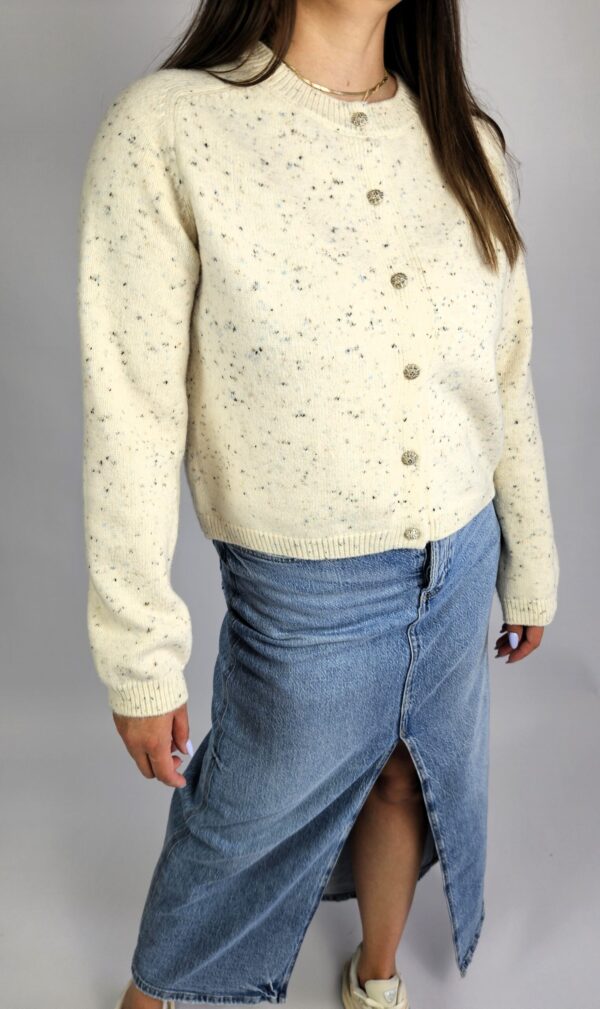 Elegancki i miękki sweter w kolorze kremowym, zapinany na guziki. Wykonany z przyjemnej w dotyku dzianiny z dodatkiem angory, która nadaje mu wyjątkową puszystość i ciepło. Doskonały na chłodniejsze dni – lekki, a jednocześnie otulający.