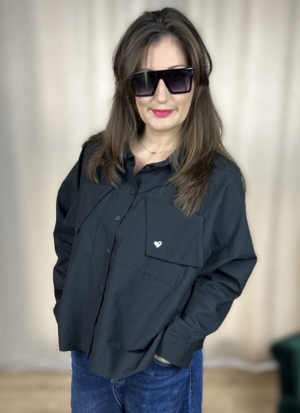 Stylowa, krótka koszula zapinana na guziki, z długim rękawem zakończonym mankietem. Na piersi dwie kieszenie z klapami, z których jedna ozdobiona jest subtelnym, wyszywanym serduszkiem. Idealna do nowoczesnych, codziennych i lekko romantycznych stylizacji.