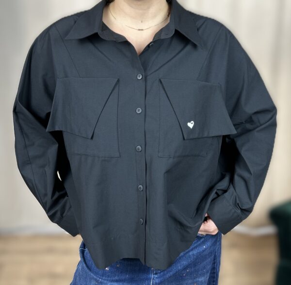 Stylowa, krótka koszula zapinana na guziki, z długim rękawem zakończonym mankietem. Na piersi dwie kieszenie z klapami, z których jedna ozdobiona jest subtelnym, wyszywanym serduszkiem. Idealna do nowoczesnych, codziennych i lekko romantycznych stylizacji.